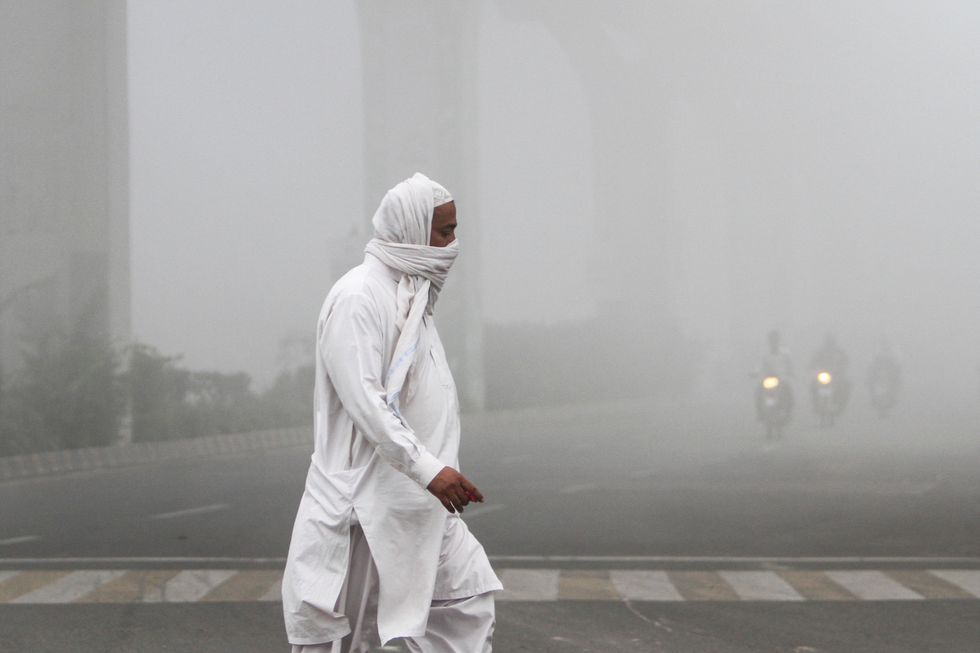A man covers his face with a scarf to avoid smog as he walks along a road in Multan, Pakistan