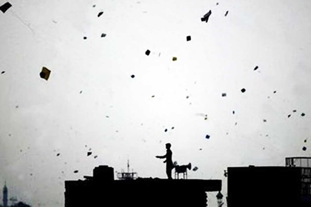 A man flies a kite from his rooftop as the sky above is filled with kites during Basant