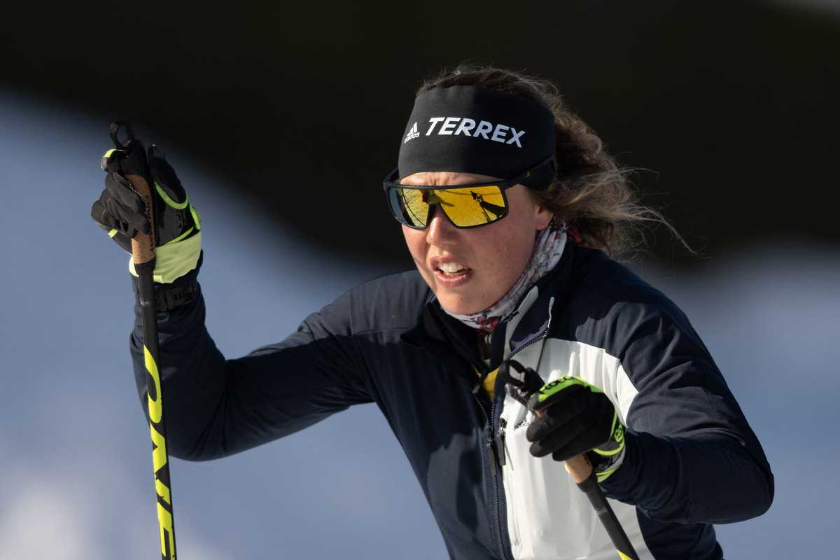 A skier with sunglasses and headband skiing on a snowy slope in sunlight.