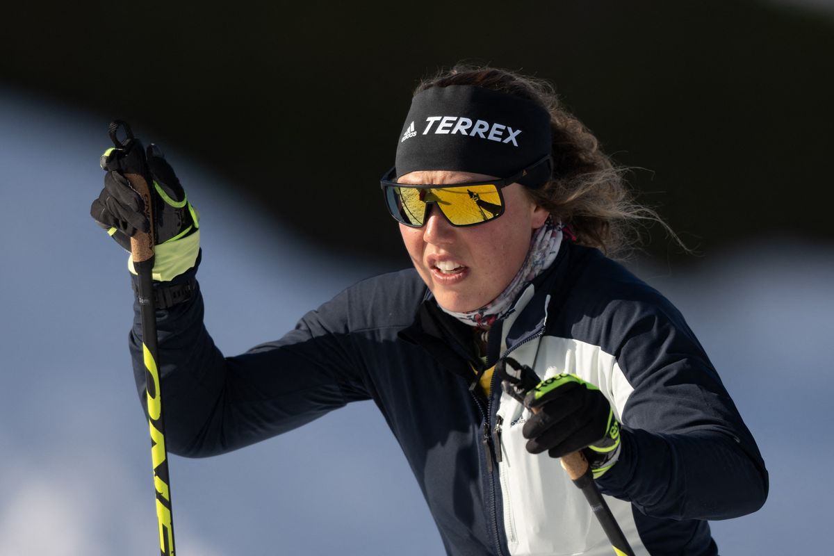 A skier with sunglasses and headband skiing on a snowy slope in sunlight.
