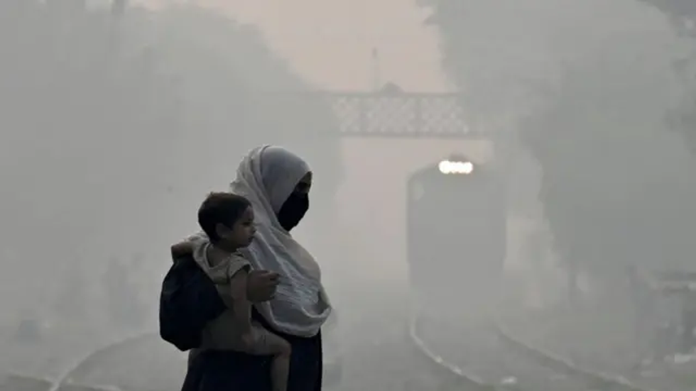 A woman carries a child as she walks across a railway track amid heavy smog in Lahore