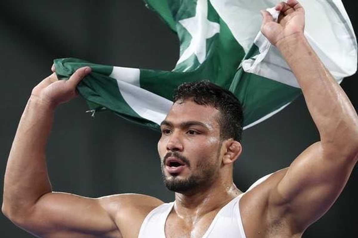Athlete celebrating with Pakistani flag raised overhead.