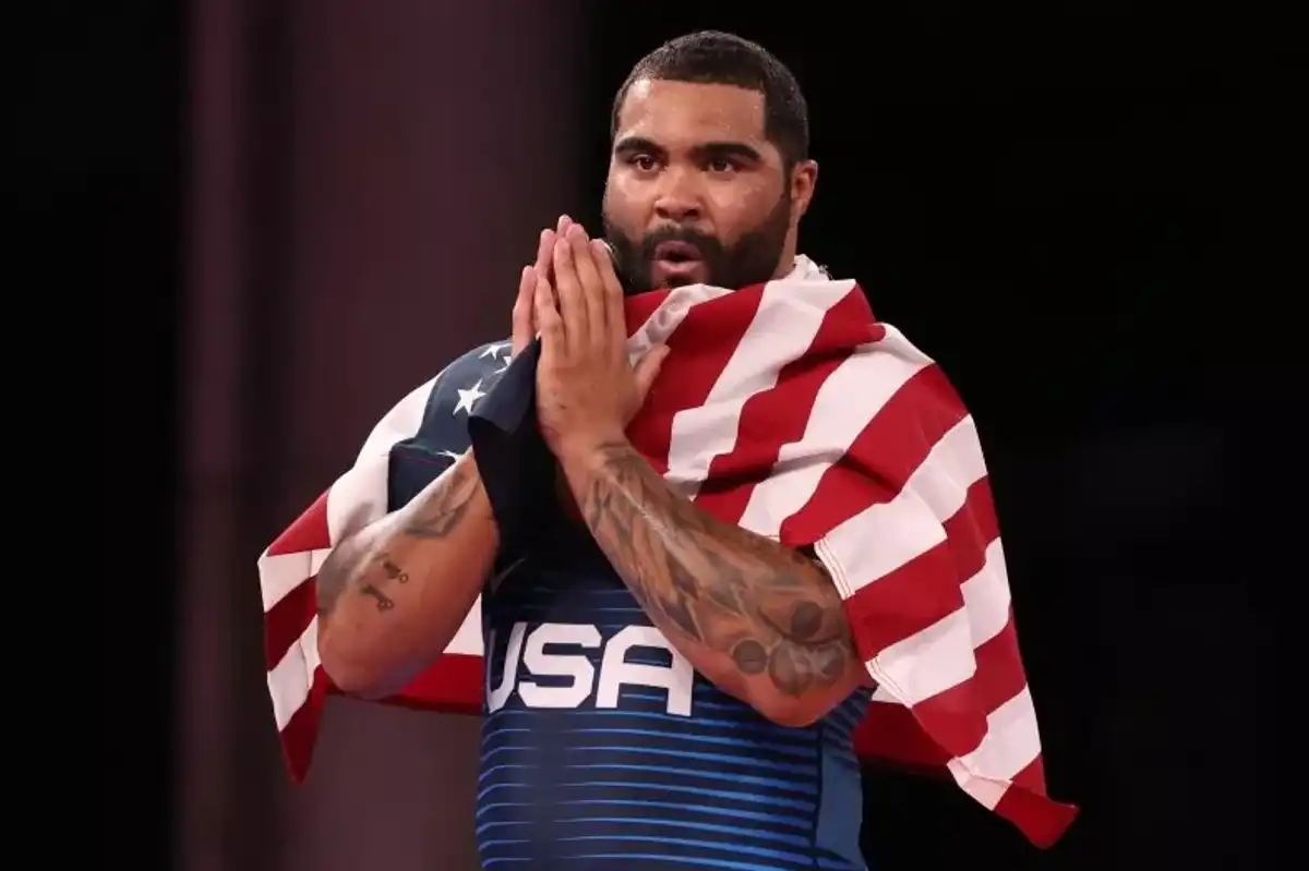 Athlete draped in American flag, clasping hands with a focused expression.
