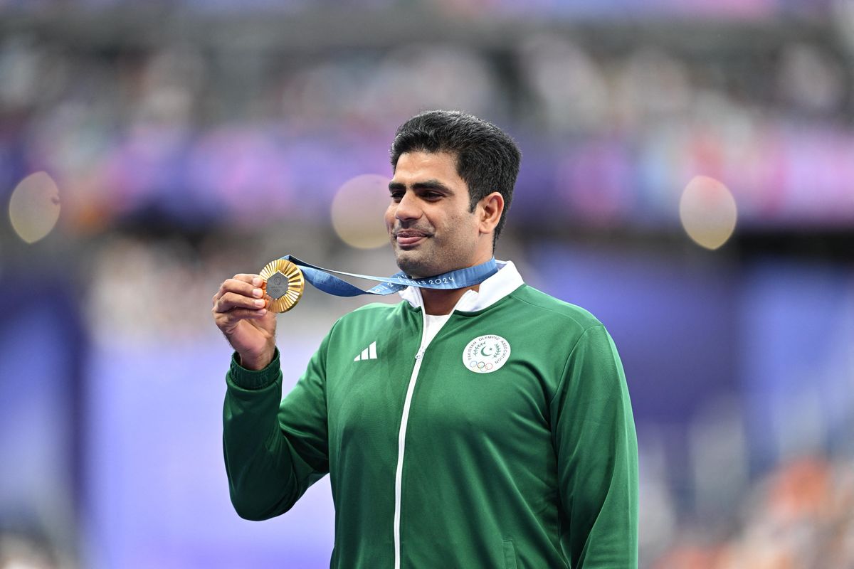 Athlete in green jacket holding a gold medal at a sports event.