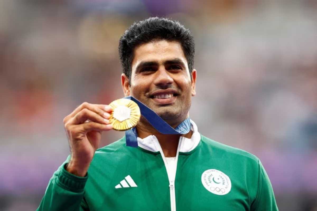 Athlete in green jacket holding a gold medal, smiling at a sports event.