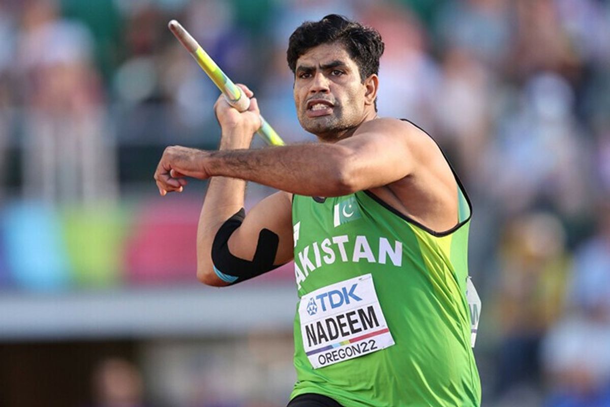 Athlete in green jersey prepares to throw a javelin at a sports event.