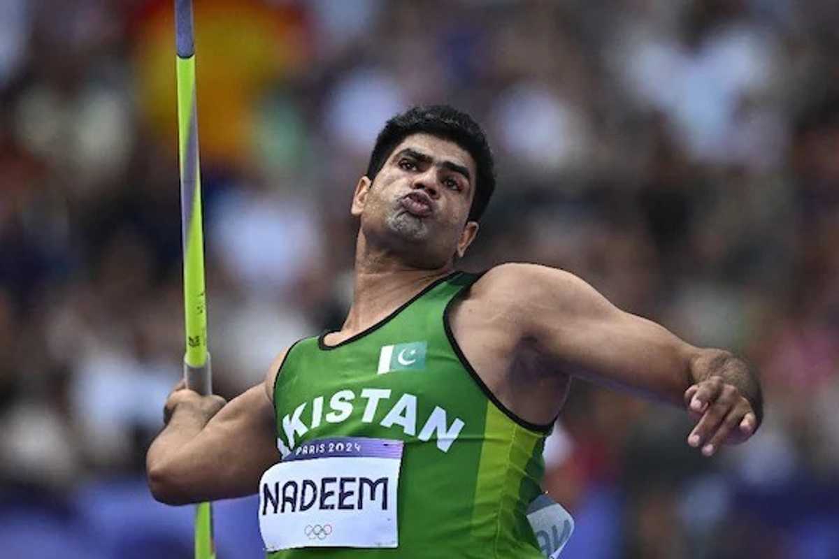 Athlete in green jersey throws a javelin at a sports event, focusing intensely.