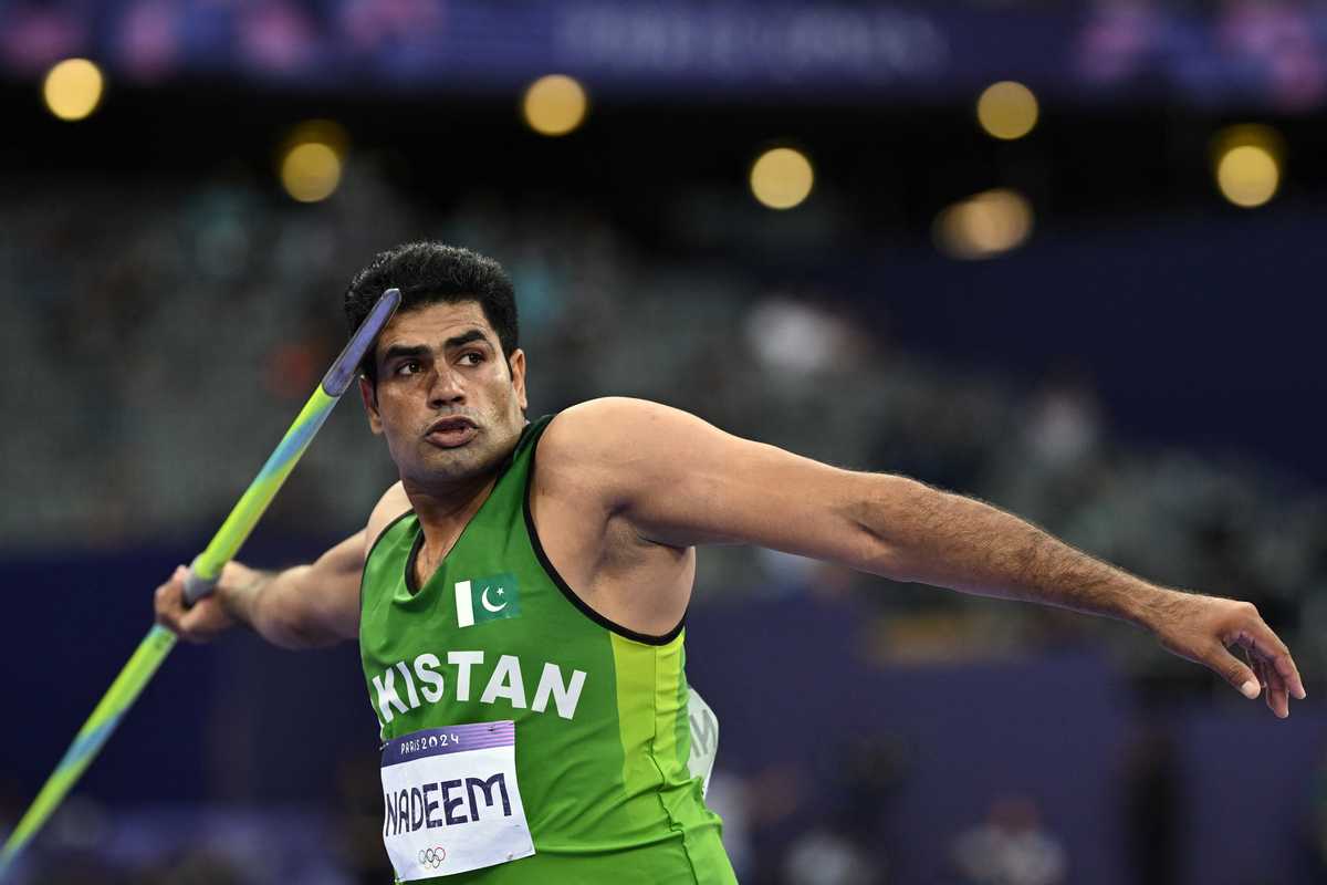 Athlete in green prepares to throw a javelin in a stadium.
