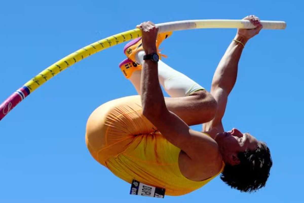 Athlete in mid-air during pole vault against clear blue sky.