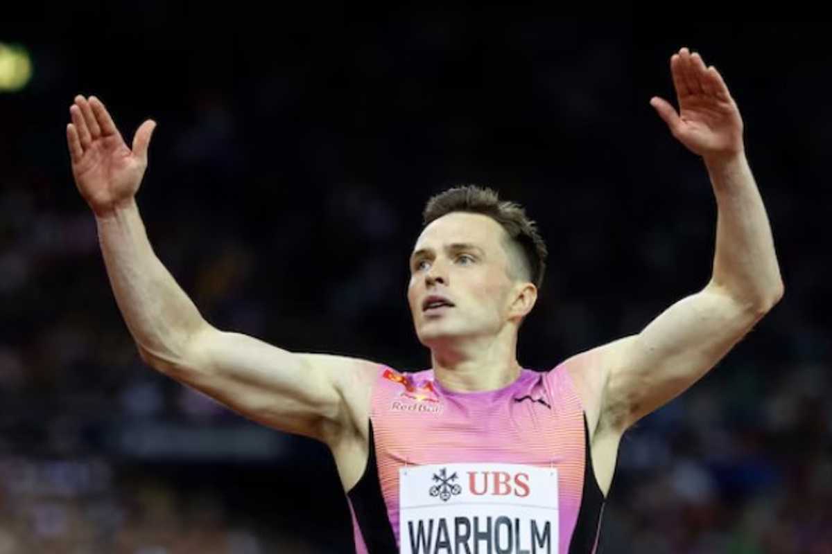 Athlete in pink jersey raising arms in triumph at a track event.