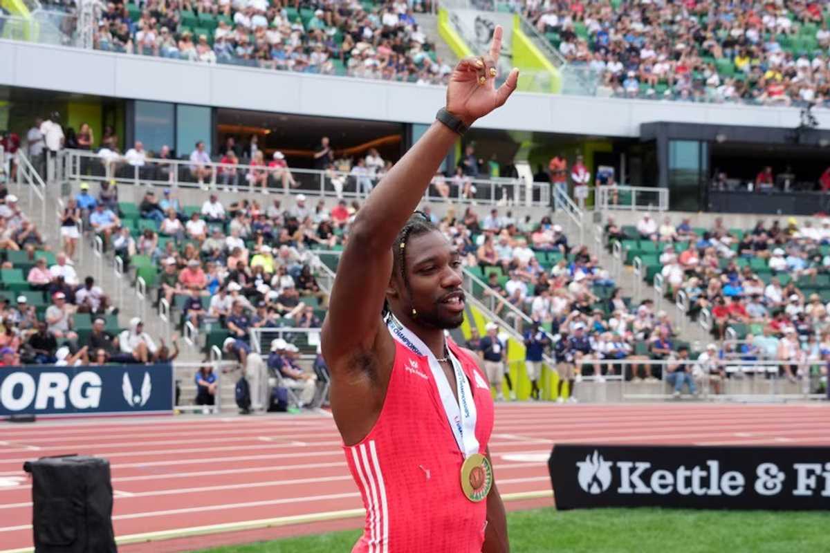 Athlete with a medal raises a hand in a stadium full of spectators.