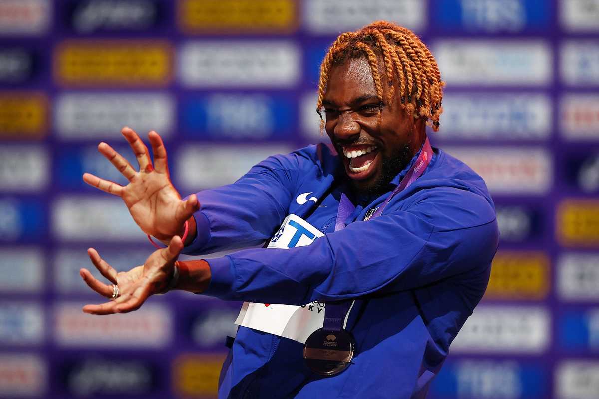 Athlete with orange hair celebrates with a smile on stage, wearing a medal.