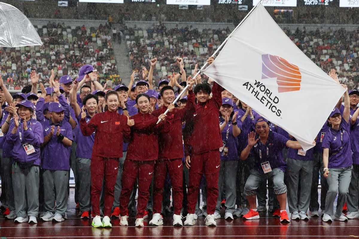 Athletes hold World Athletics flag, surrounded by cheering crowd in stadium.