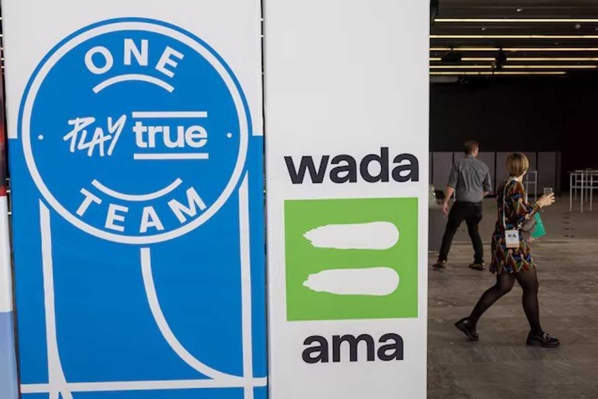 Blue "Play True" and green "WADA AMA" signs with people walking past.
