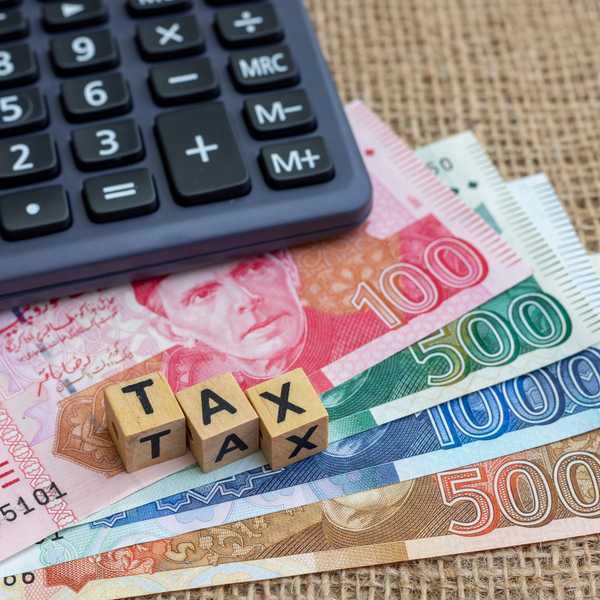 Calculator and wooden blocks spelling "TAX" on banknotes background.