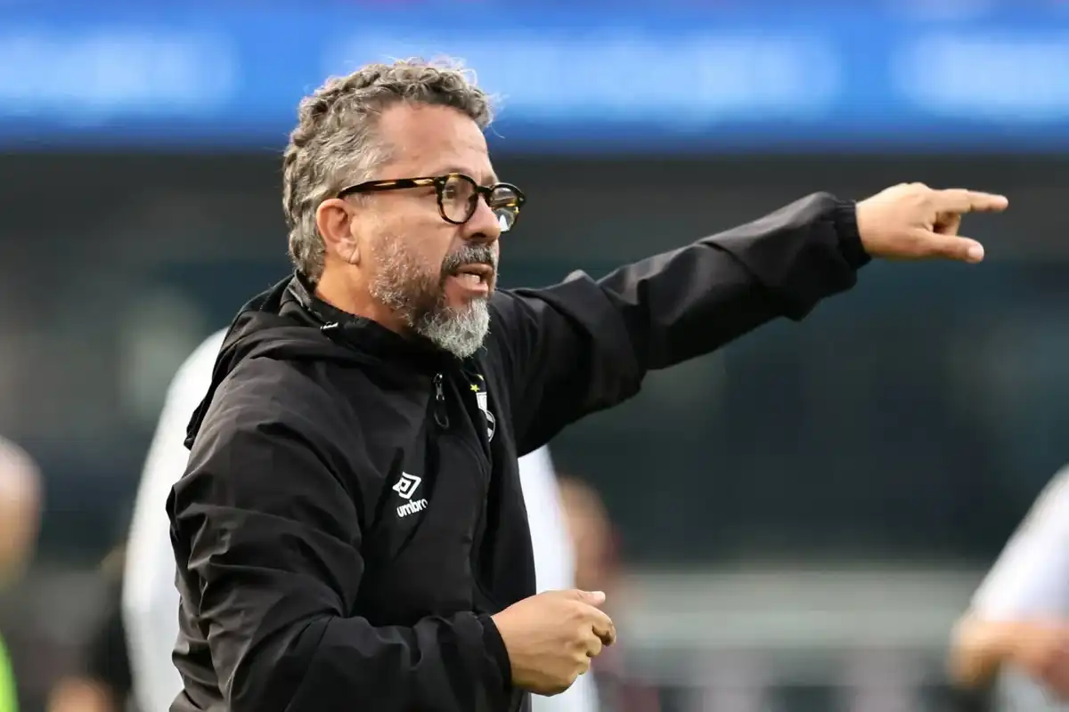 Coach gesturing passionately during a game, wearing a black jacket and glasses.
