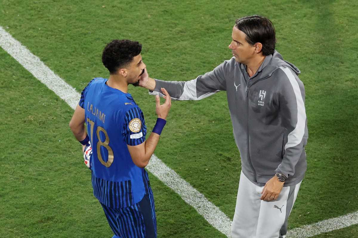 Coach talks to a player in blue jersey on a soccer field.