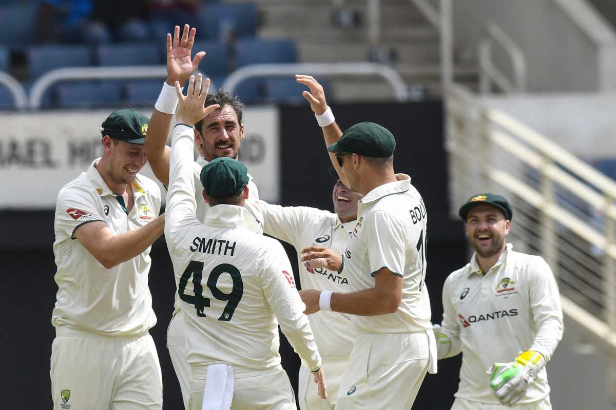 Cricket players celebrate on the field, wearing white uniforms and green caps.