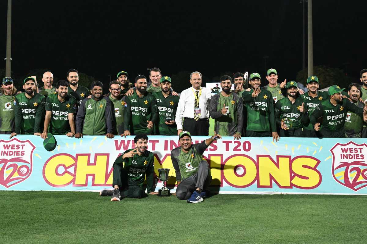 Cricket team celebrates T20 victory, standing behind "Champions" banner on the field.