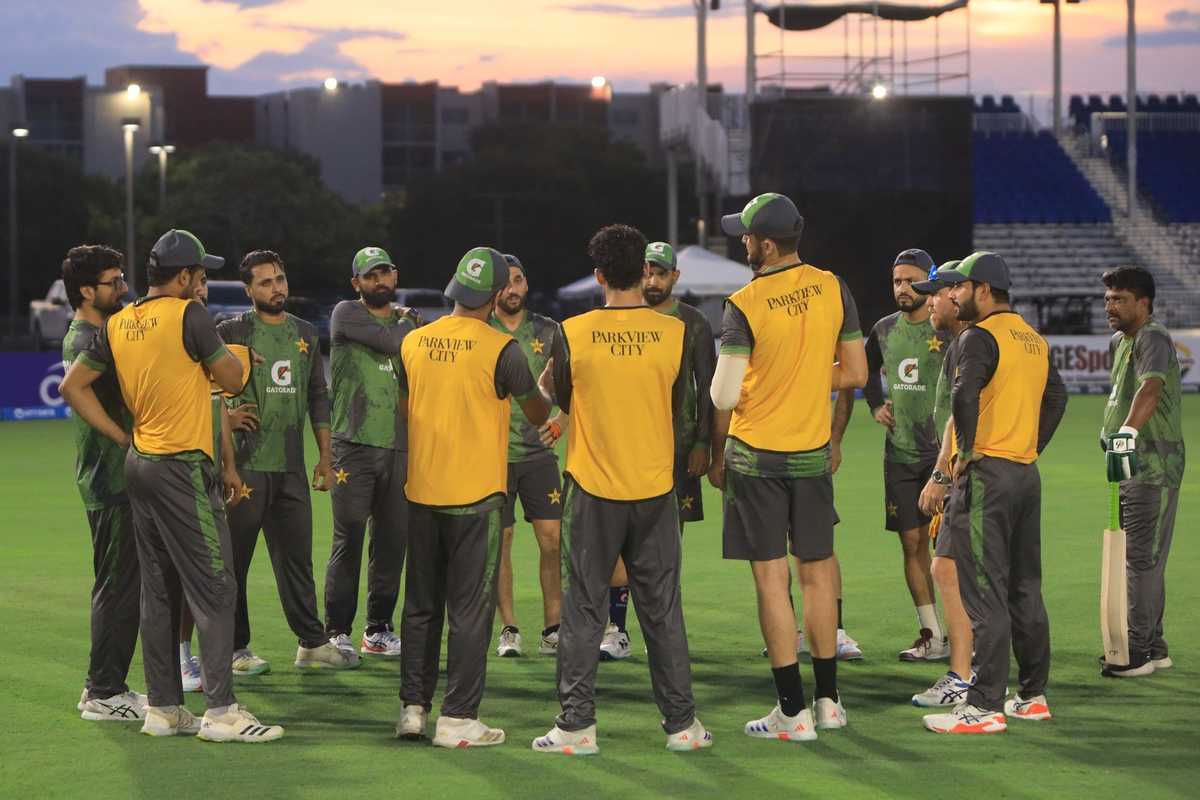 Cricket team huddling on the field during sunset, wearing green and yellow uniforms.