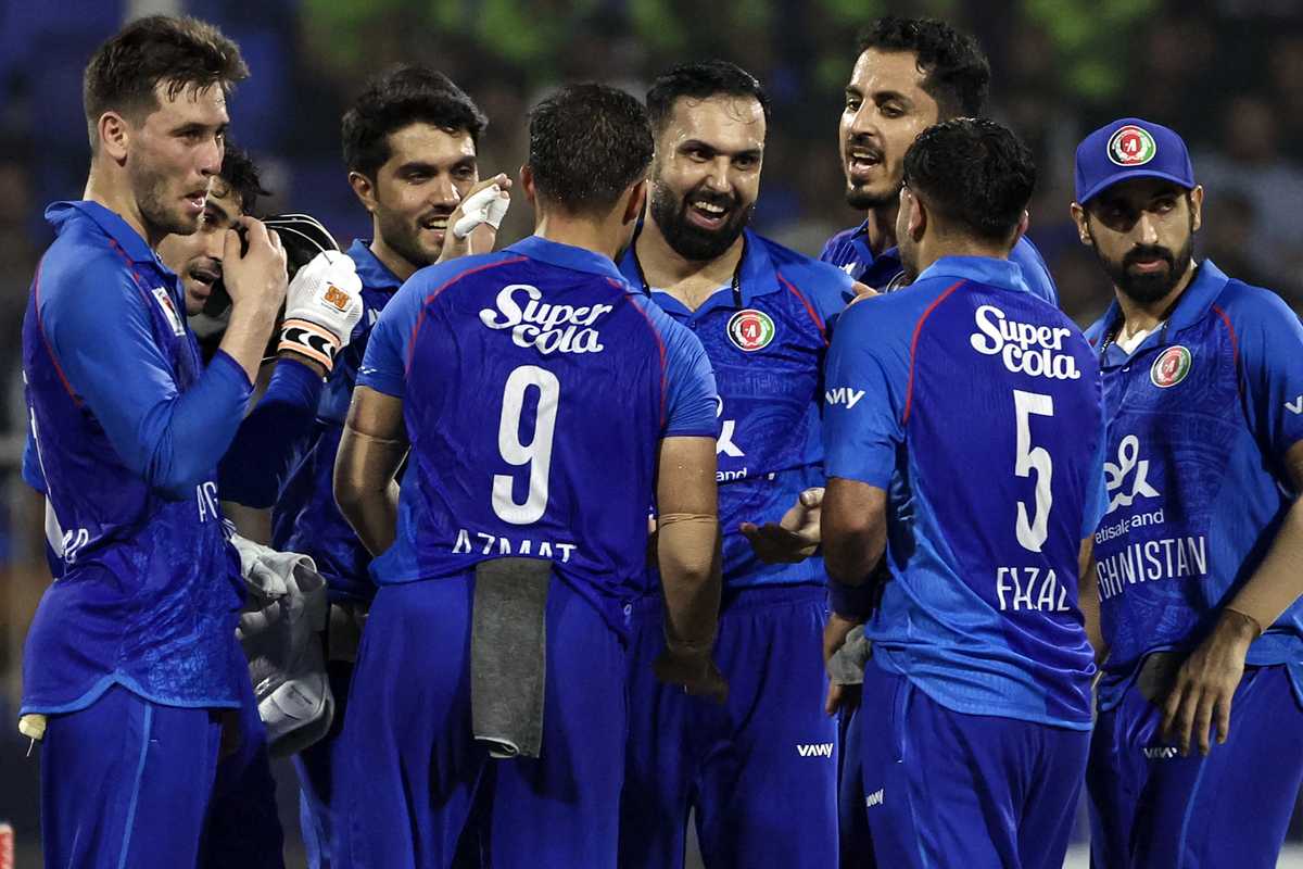 Cricket team in blue jerseys celebrating on the field.