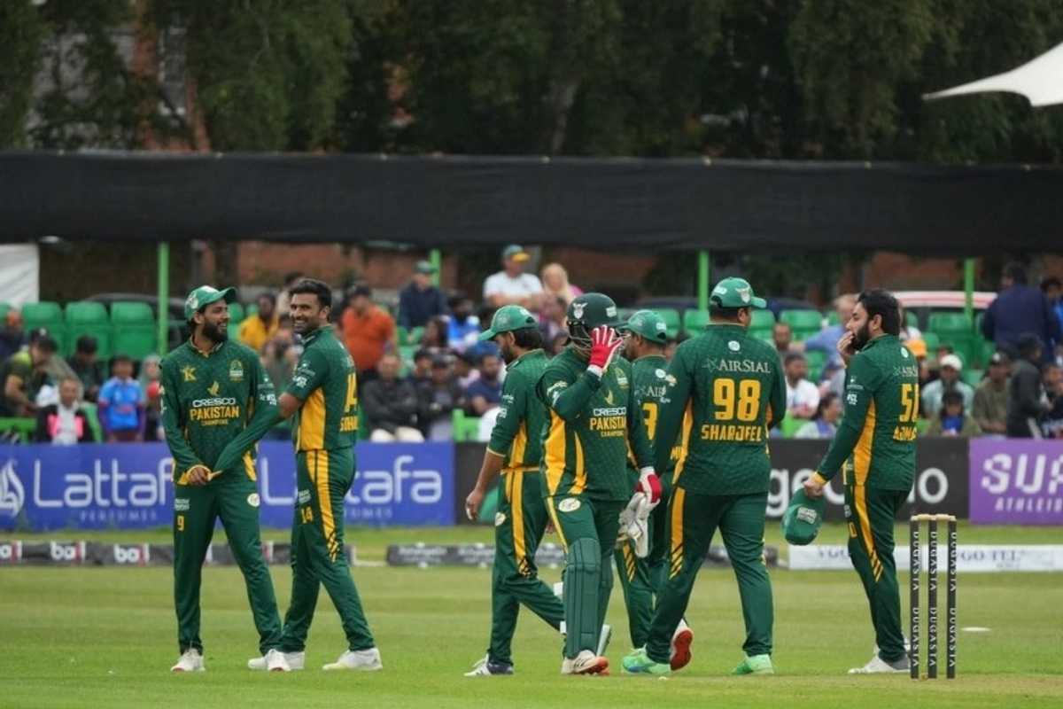 Cricket team in green uniforms celebrates on the field, with stumps and crowd behind.