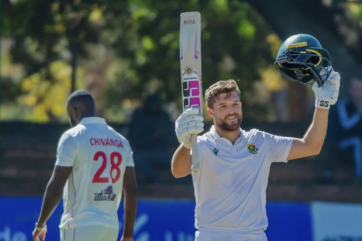 Cricketer celebrating a milestone with bat and helmet raised.