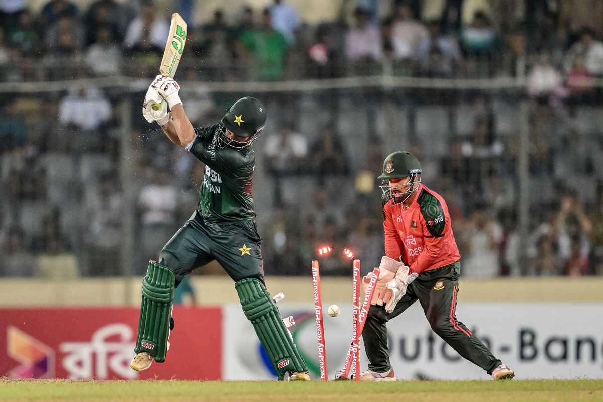 Cricketer is bowled, stumps shattered by incoming ball; wicketkeeper stands ready.