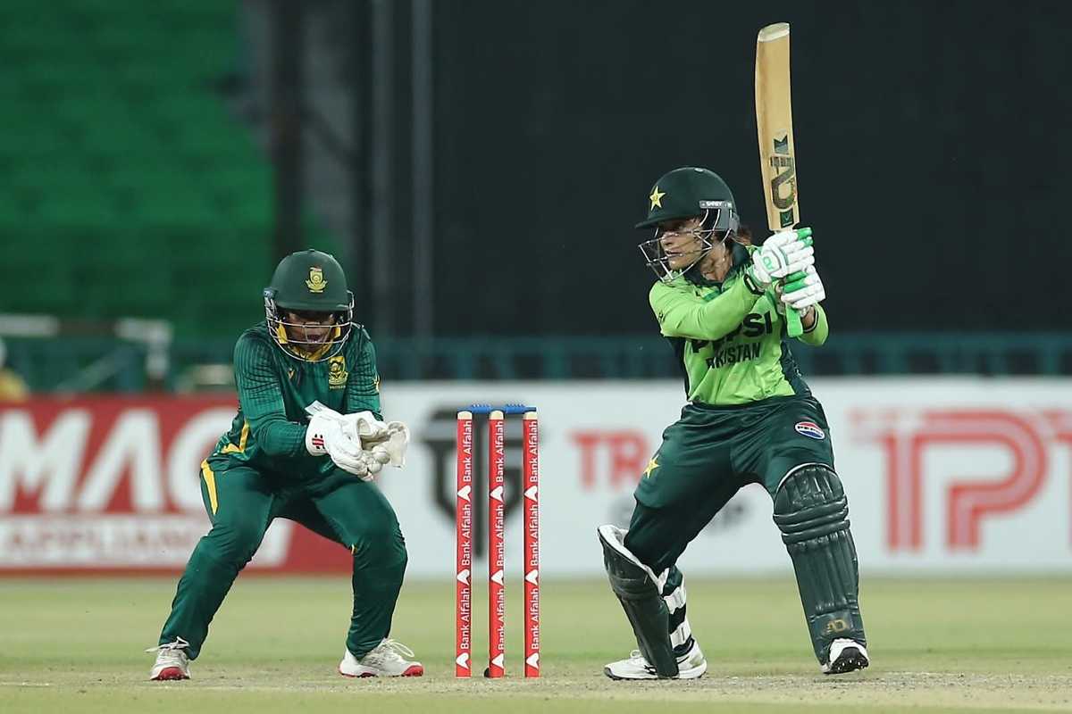 Cricketer plays a shot as the wicketkeeper crouches behind stumps during a match.