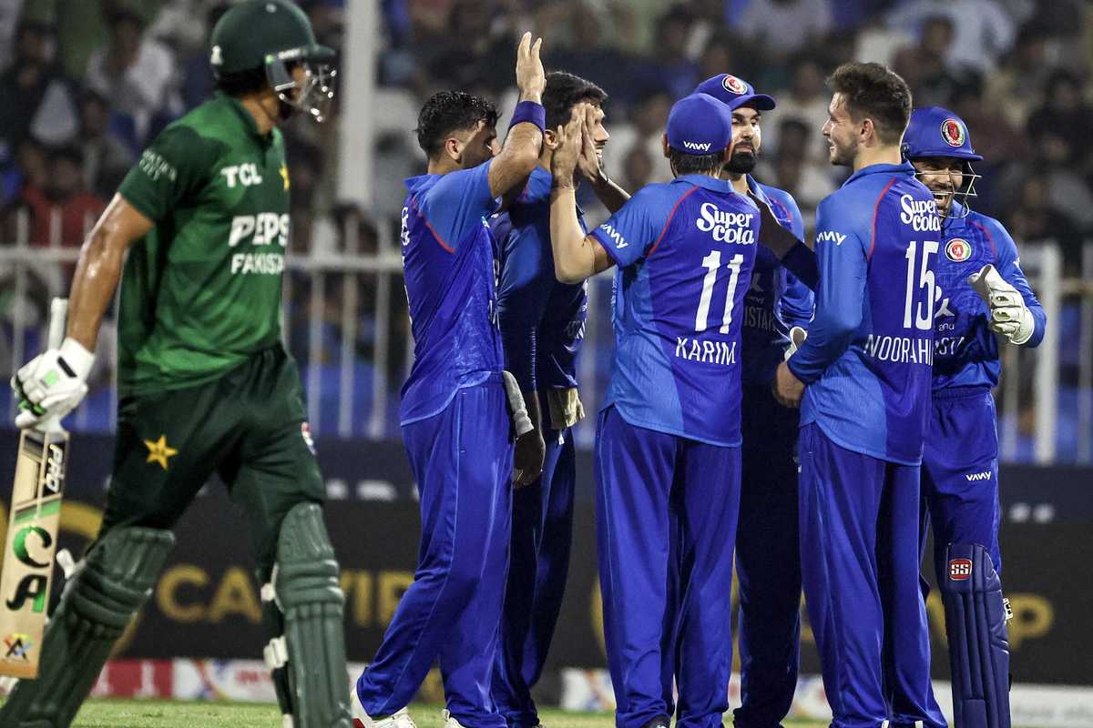 Cricketers in blue celebrating a wicket during a match against a player in green.