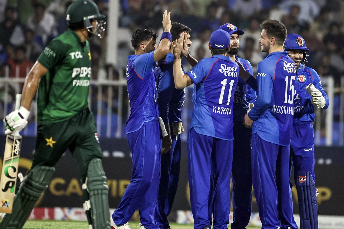 Cricketers in blue celebrating a wicket during a match against a player in green.