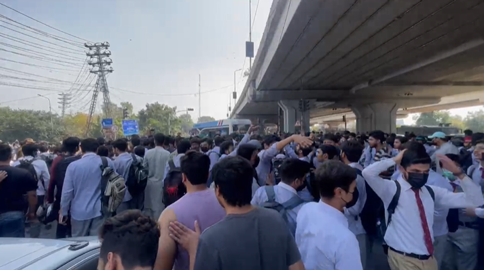 Crowd of people gather under an overpass on a sunny day.