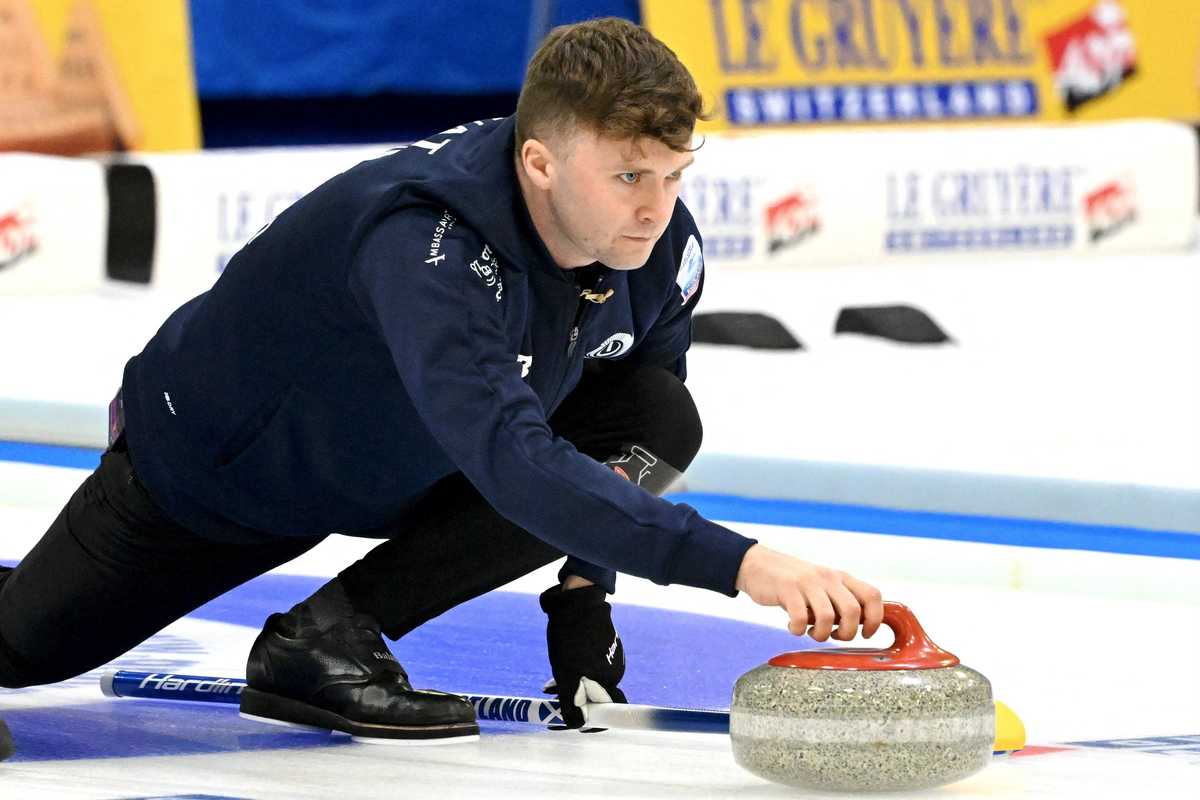 Curler in action sliding a stone on ice, Le Gruyère banner in background.