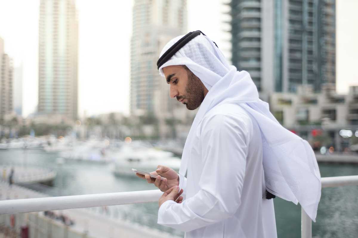 Emirati Man standing on terrace in Dubai Marina and checking his mobile