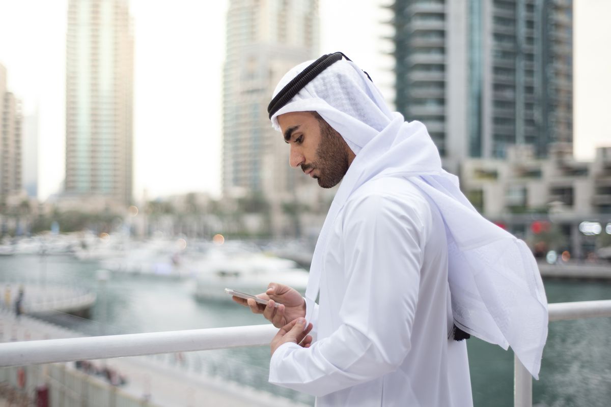 Emirati Man standing on terrace in Dubai Marina and checking his mobile