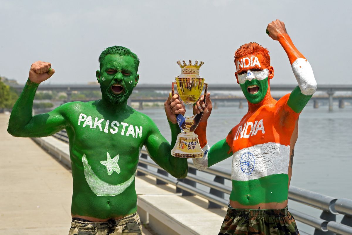 Fans painted as Pakistan and India cheer with a trophy by a riverside.