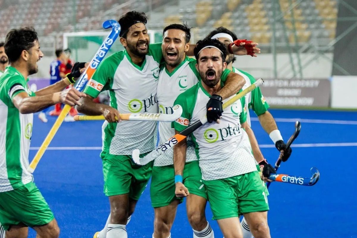 Field hockey players in green jerseys celebrate energetically on a blue turf.