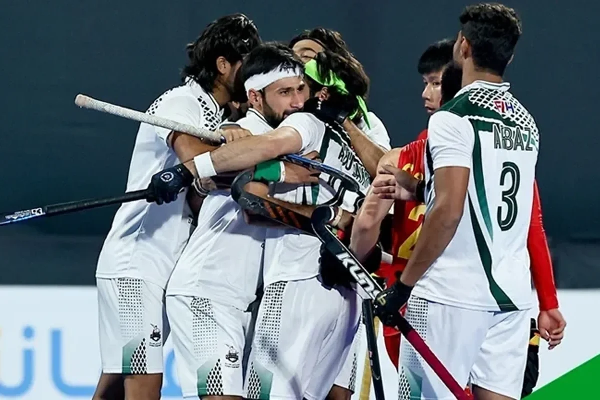 Field hockey players in white uniforms celebrating and hugging on the field.