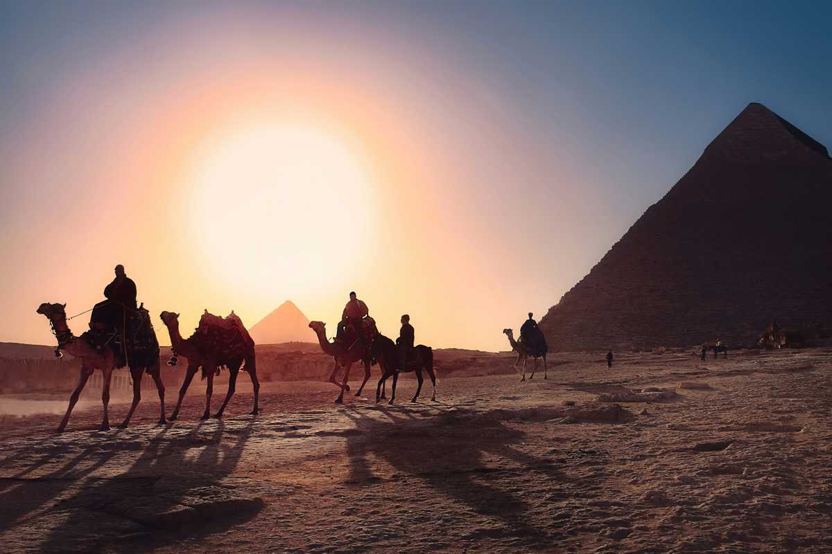 Five persons riding camels walking on sand beside Pyramid of Egypt