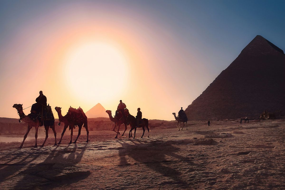 Five persons riding camels walking on sand beside Pyramid of Egypt