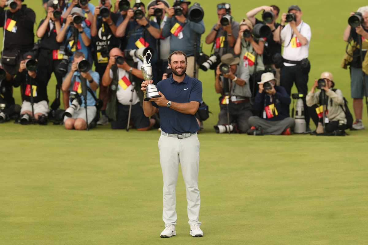 Golfer holding a trophy on a green, surrounded by photographers capturing the moment.