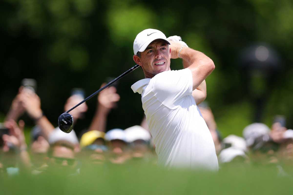 Golfer in a white shirt swings a club with spectators in the background.