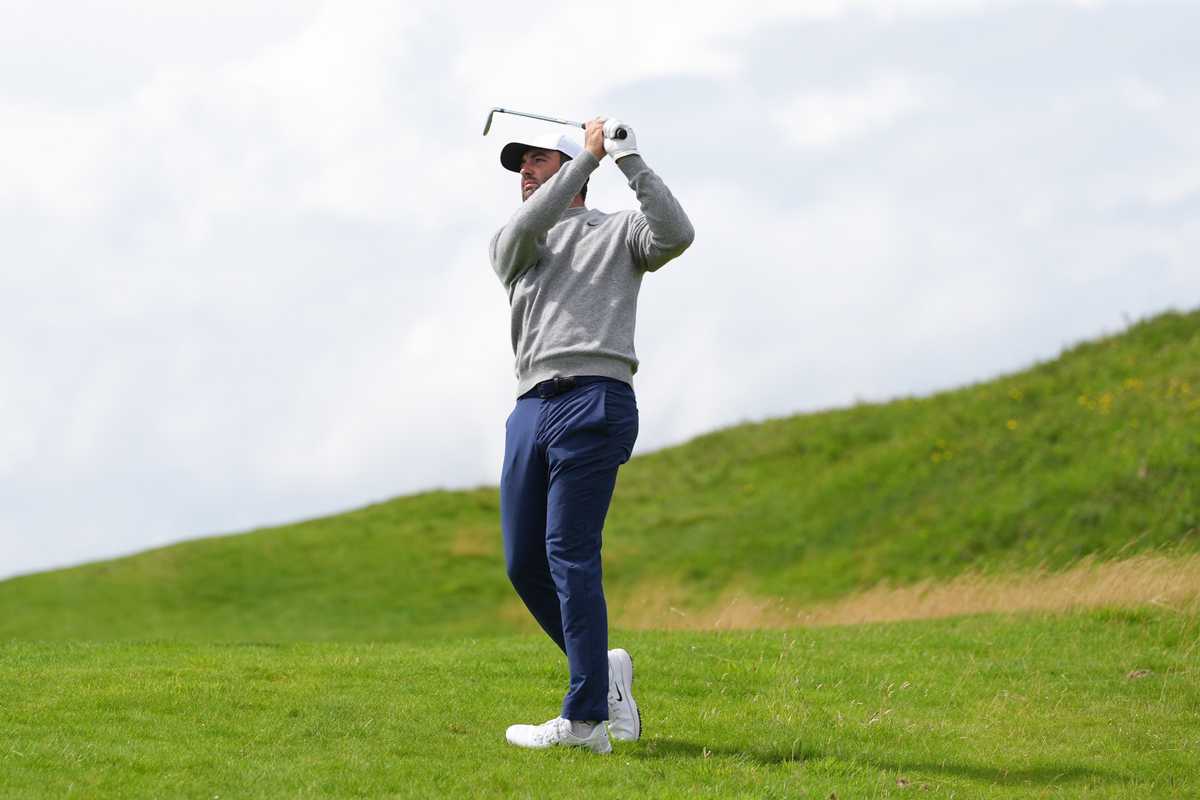 Golfer in mid-swing on a sunny golf course with green hills in the background.