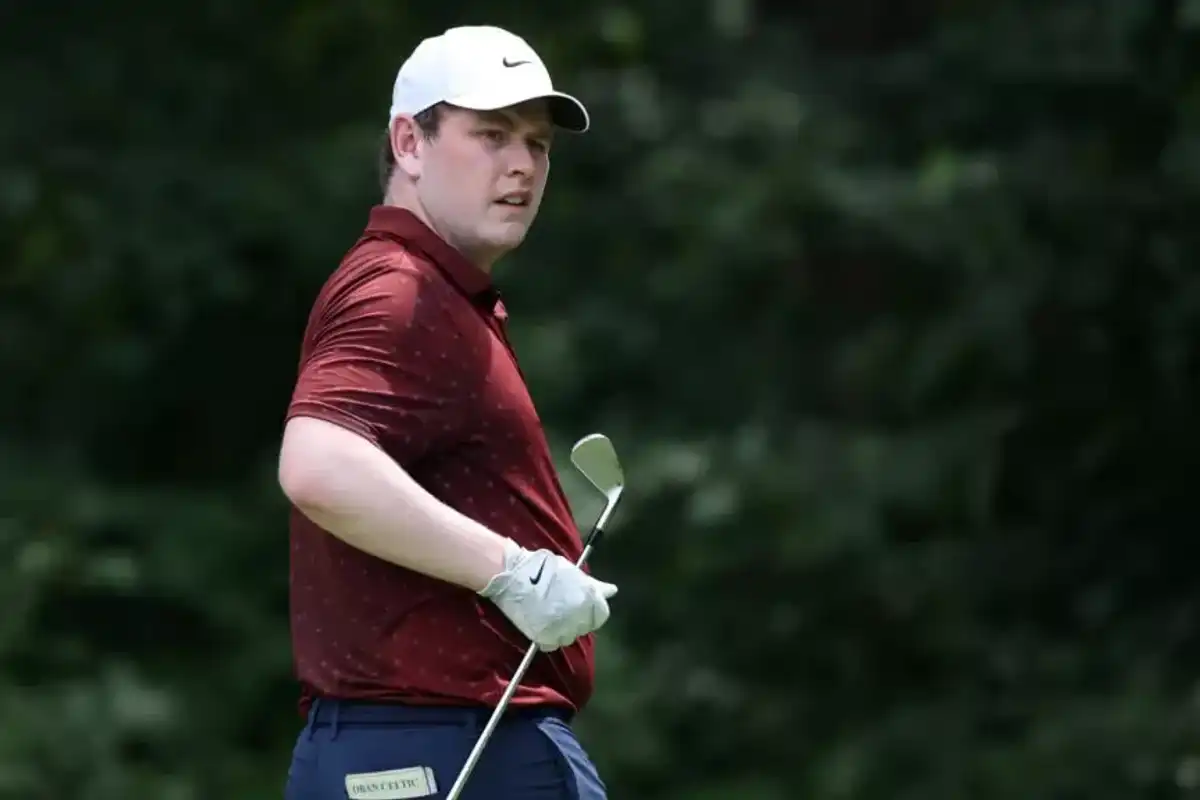 Golfer in red shirt and cap holding a club, standing outdoors.