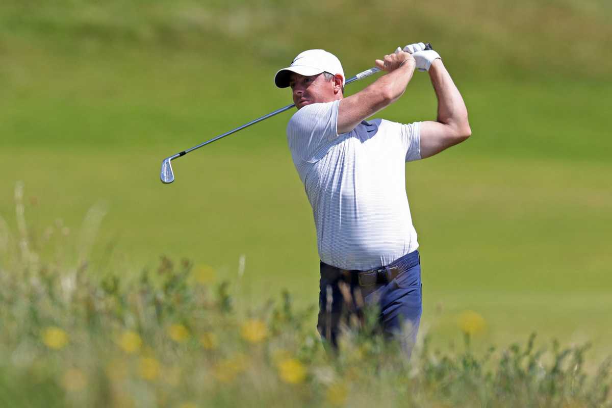 Golfer in white cap swinging club on a green fairway.
