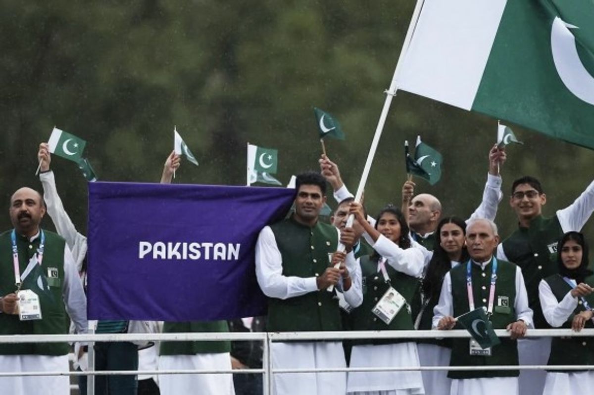 Group of people waving Pakistan flags at an outdoor event, one holding a large flag.