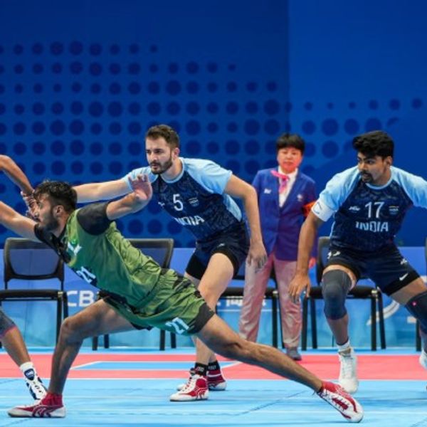 Kabaddi match action; players in mid-movement on a blue court.