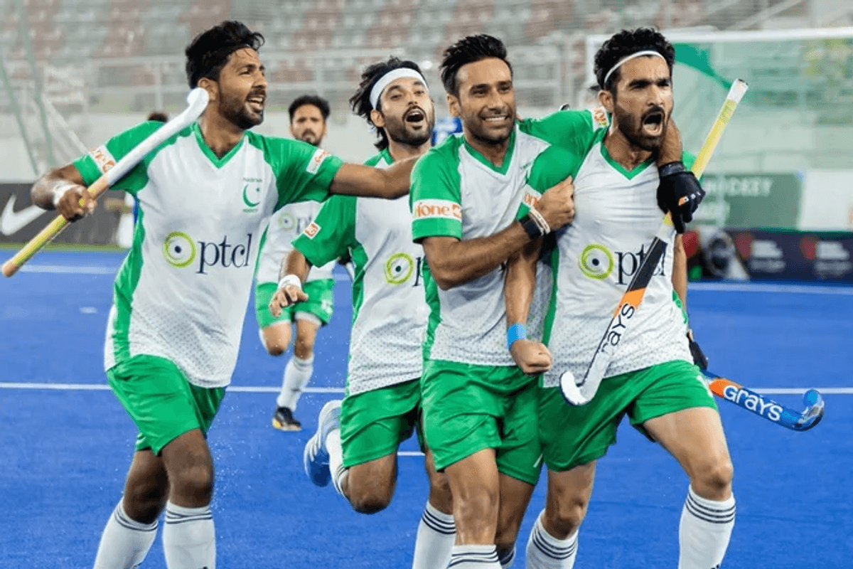 Male field hockey players celebrating on a blue pitch in green and white uniforms.