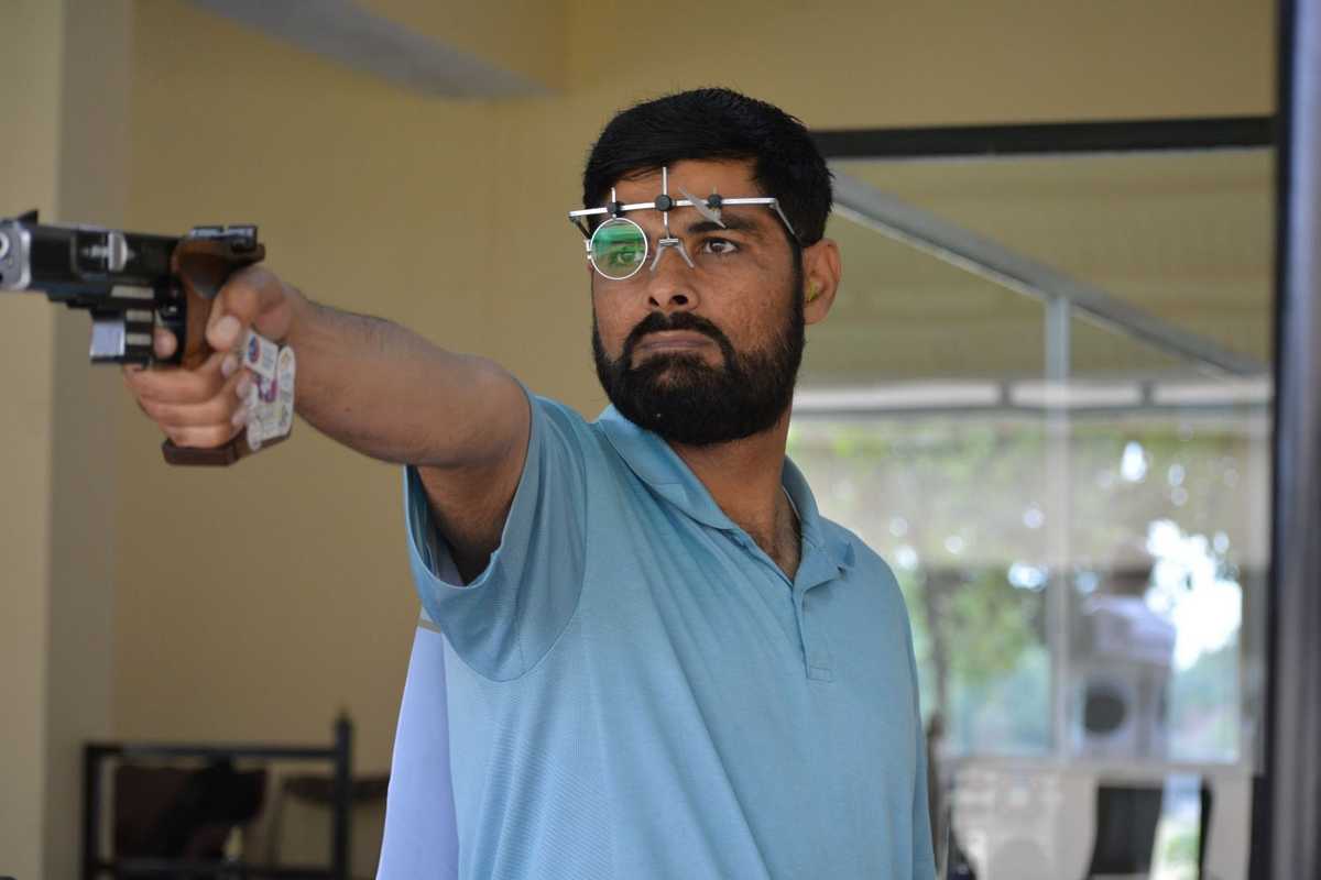 Man aiming a pistol with shooting glasses in an indoor range.