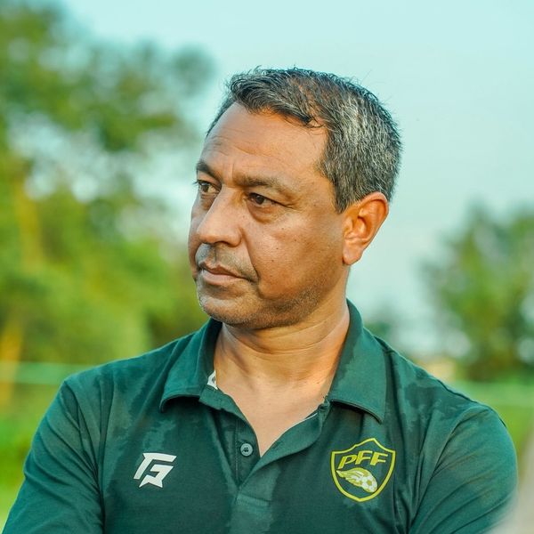 Man in a green shirt pensively gazing to the side, with blurred greenery in the background.